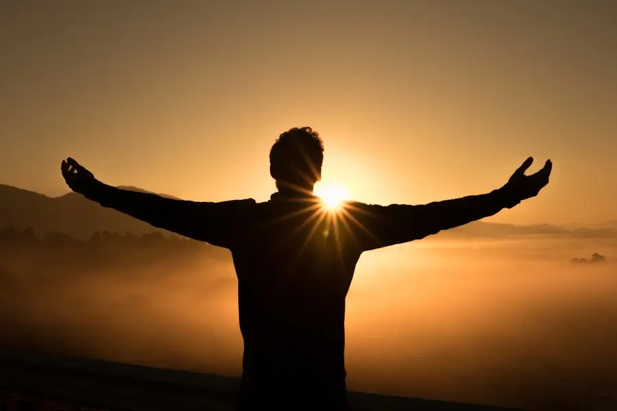 Persona con los brazos abiertos frente al amanecer